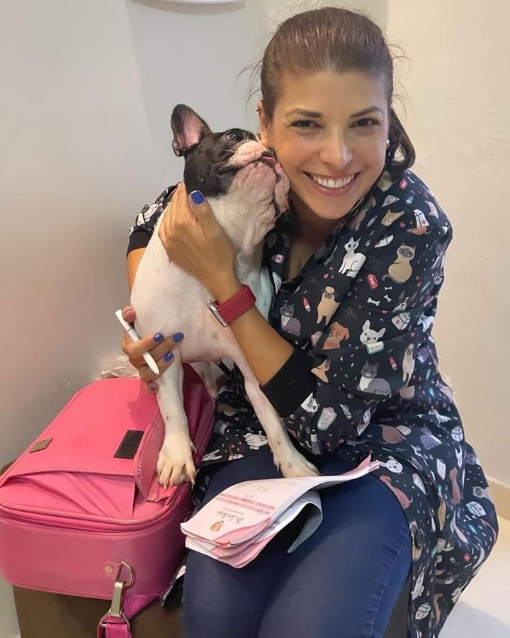 Dra. Sara Burrini recebendo lambeijo de um buldogue francês durante o atendimento