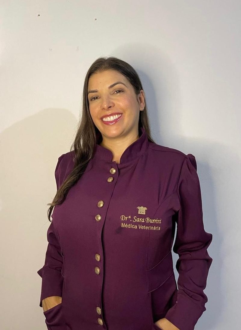 Dra. Sara Burrini, médica veterinária, sorrindo de jaleco bordô